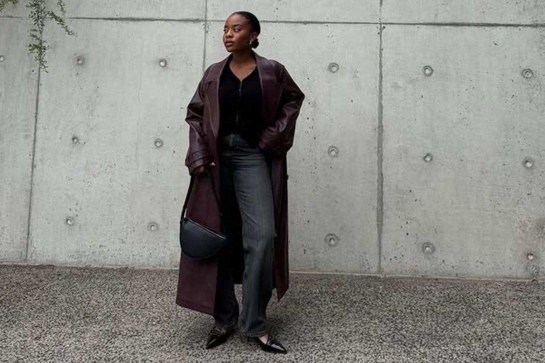 Woman dressed in black with maroon trench coat posing in front of concrete wall